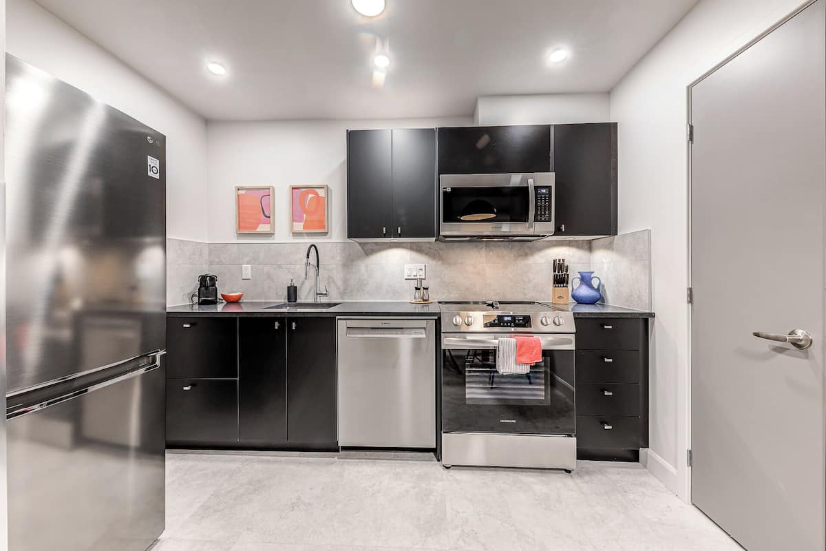 A modern kitchen with stainless steel appliances, black cabinets, and a microwave.
