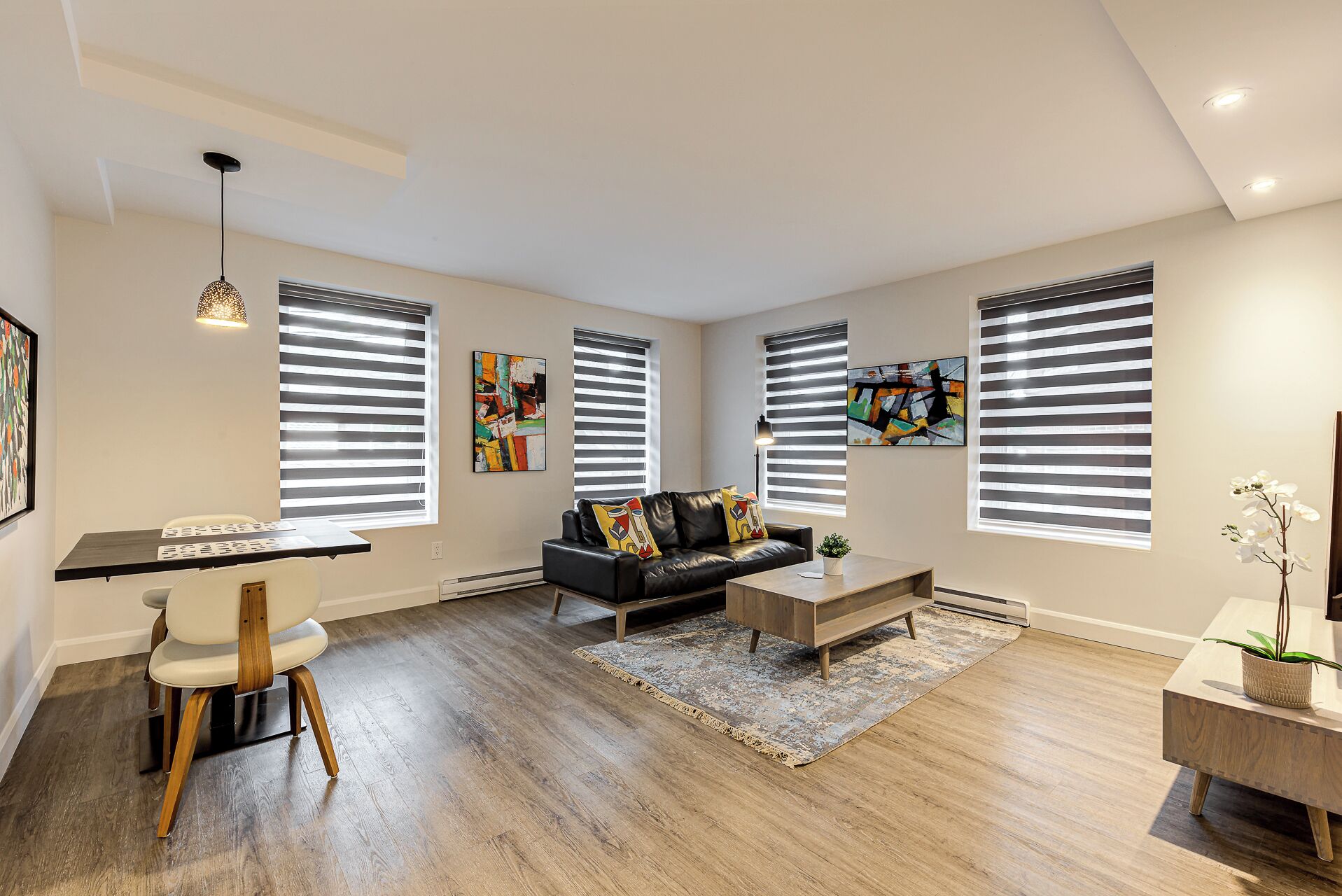 A modern living room with a black leather sofa, a wooden coffee table, and a dining area with a white chair and a wooden table.