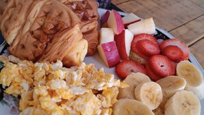 A plate with scrambled eggs, pancakes, sliced bananas, strawberries, and a cup of coffee. - Adventure hostel (San Gil)