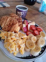 Un plato con huevos revueltos, tortitas, rodajas de plátano, fresas y una taza de café.