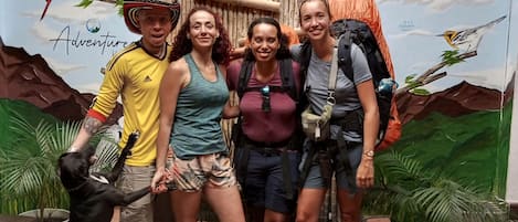 Un grupo de personas posando frente a un mural con temática de jungla, que incluye un tablero de ajedrez en el suelo.