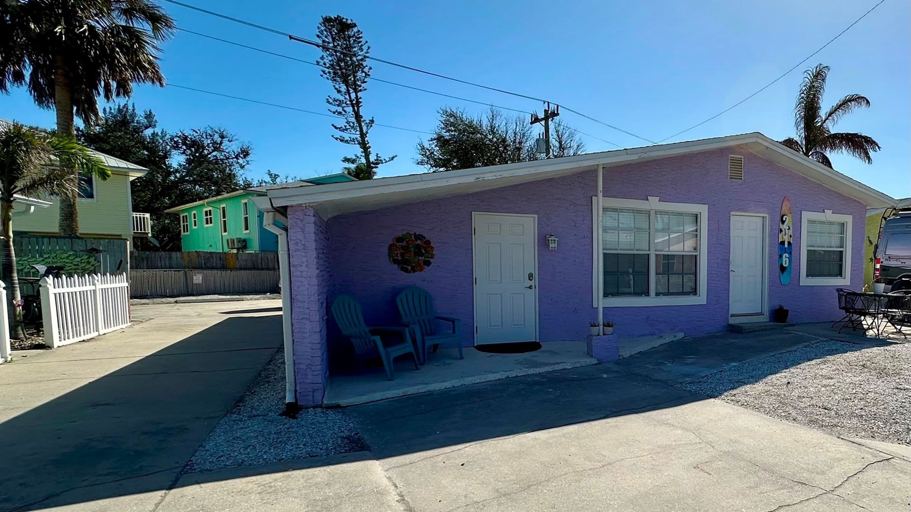 A single-story building with a purple exterior, a front door, and a small porch with two chairs.
