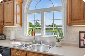 A kitchen with wooden cabinets, a double sink, and a large window with a view of a lake.