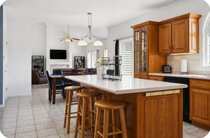 A kitchen with wooden cabinets, a large island with stools, a ceiling fan, and a flat-screen TV.