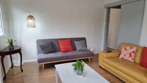 A modern living room with a grey sofa, a yellow sofa, a white coffee table, and a hanging light fixture. - Relax in a cozy house,BBQ,10 mins from the beaches (Miranda)