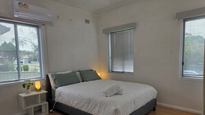 A bedroom with a bed, bedside tables, a lamp, and windows. - Relax in a cozy house,BBQ,10 mins from the beaches (Miranda)