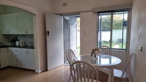 A modern kitchen with white cabinets and a dining area with a round glass table and white chairs. - Relax in a cozy house,BBQ,10 mins from the beaches (Miranda)