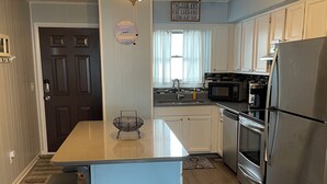 Una cocina con una isla central, electrodomésticos de acero inoxidable, un ventilador de techo y un reloj en la pared.
