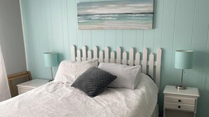 Un dormitorio con una cama, dos mesitas de noche, un cuadro colgado en la pared y un cabecero de madera blanca.