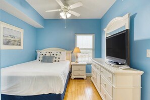 A bedroom with a bed, a nightstand, a lamp, a dresser, a TV, and a ceiling fan.