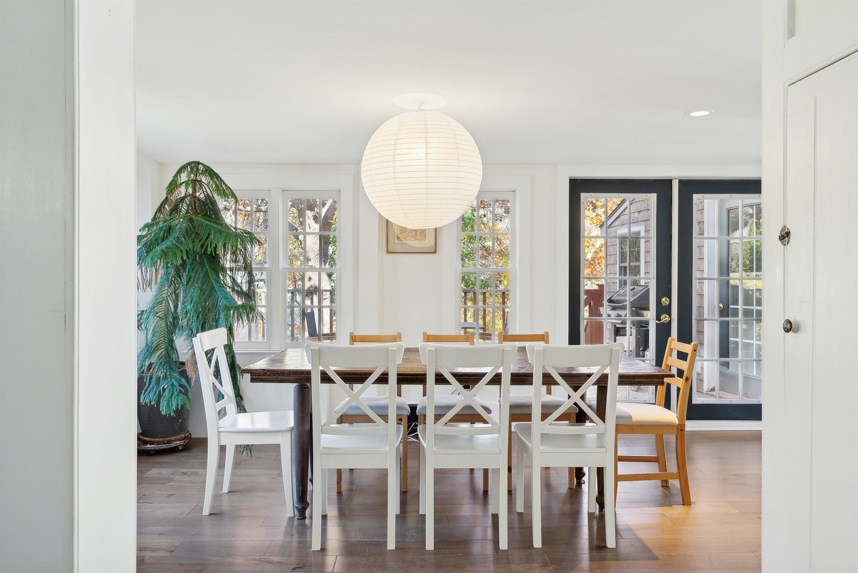Un coin repas avec une table et des chaises blanches, un luminaire suspendu et une grande plante.