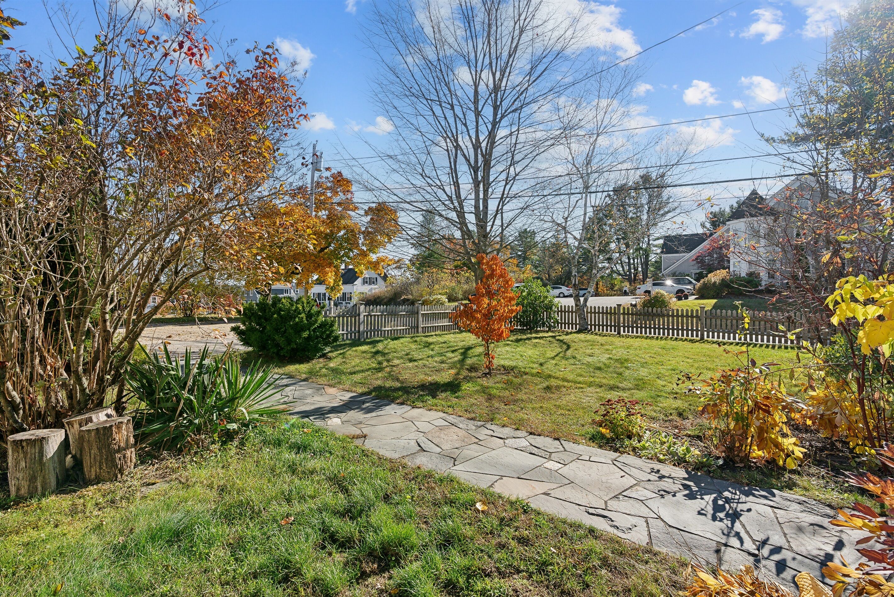 A residential area with a stone pathway, autumn foliage, and a wooden fence.