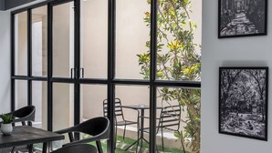 Une chambre moderne dotée d’une grande porte-fenêtre coulissante donnant sur un jardin. À l’intérieur, on trouve une table avec des chaises et une plante en pot.