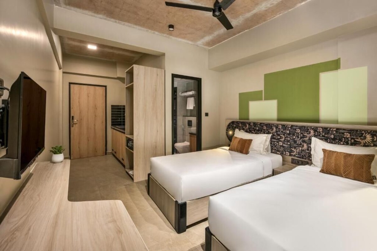 Een hotelkamer met twee bedden, een kledingkast, een badkamer en een plafondventilator.