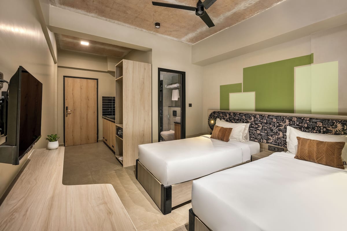 Une chambre d’hôtel moderne équipée de deux lits, d’une armoire, d’une salle de bain et d’un ventilateur de plafond.