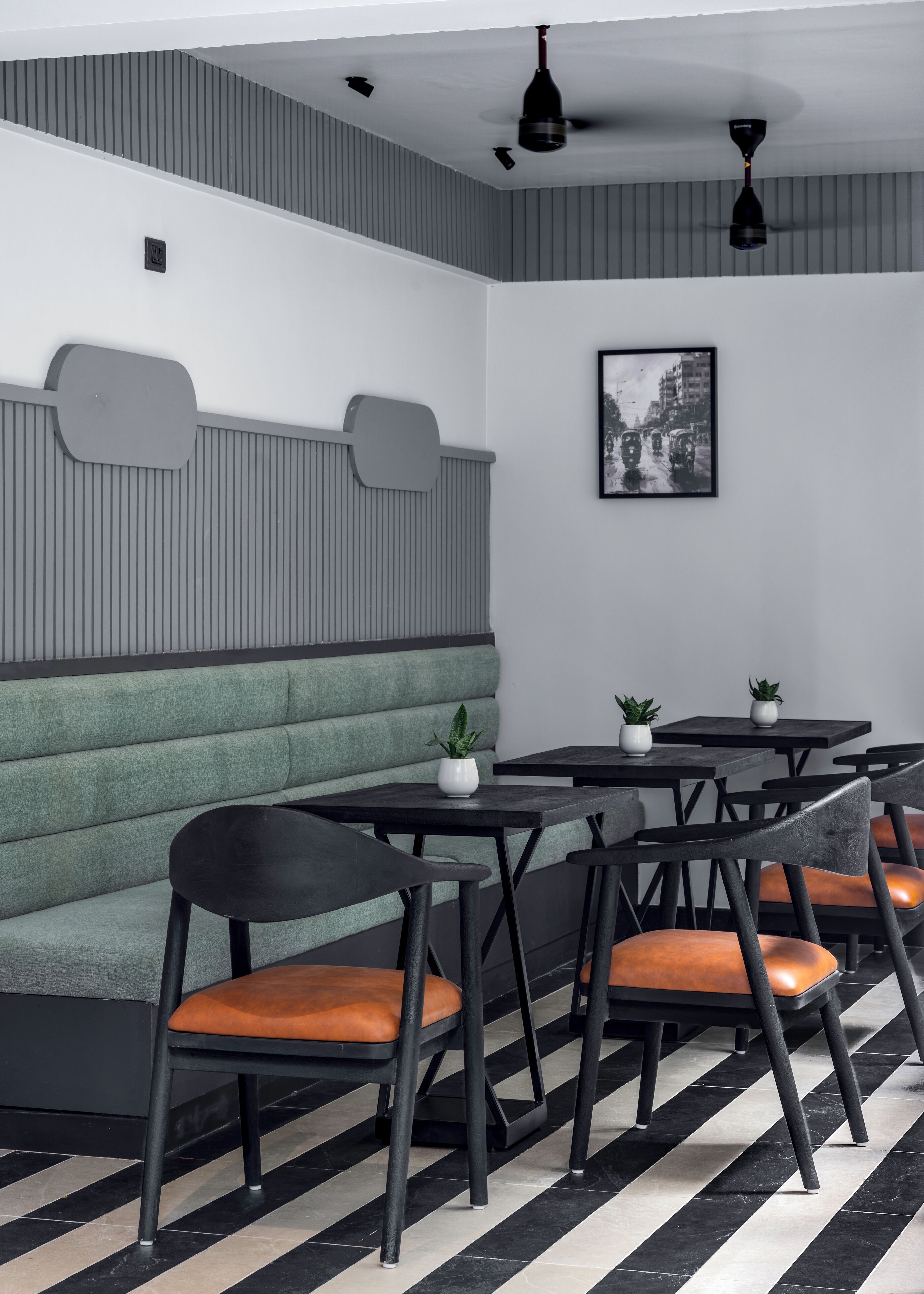 Un intérieur moderne avec un banc recouvert d’un tissu vert, des chaises et des tables noires, et un sol à carreaux noirs et blancs.