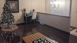 Una sala de estar con una mesa de centro de madera, un árbol de Navidad, un cuadro enmarcado y una ventana con persianas.