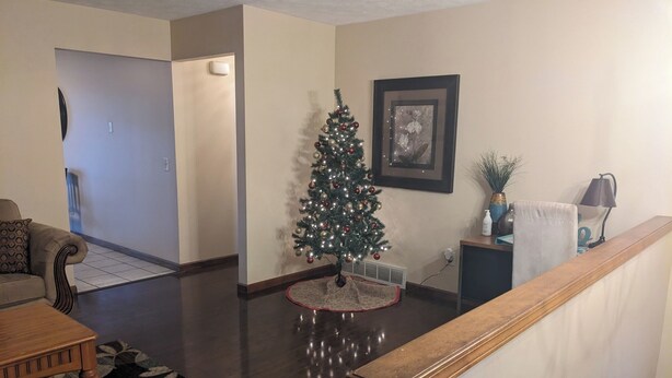 Una sala de estar con una mesa de centro de madera, un tapete estampado, un árbol de Navidad y un cuadro en la pared.