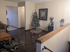 Un salon avec une table basse en bois, un tapis à motifs, un sapin de Noël et un tableau encadré accroché au mur.