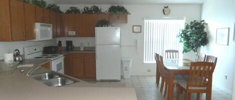 A kitchen with wooden cabinets, a white refrigerator, and a dining area with wooden chairs and a table.