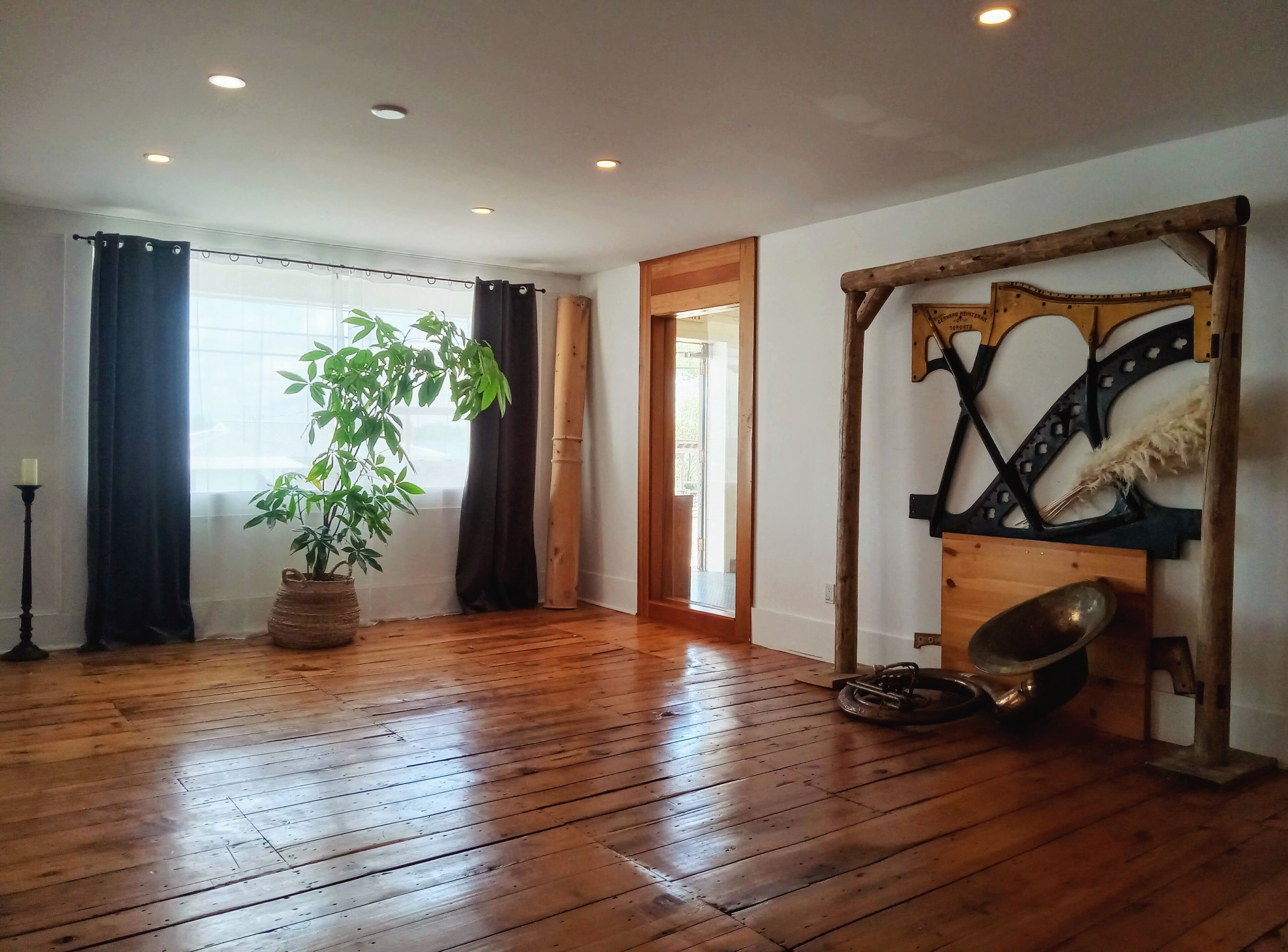 Una habitación amplia con suelo de madera, una planta grande en maceta, un tradicional panel japonés shoji y una estructura de madera rústica con un abanico colgante.