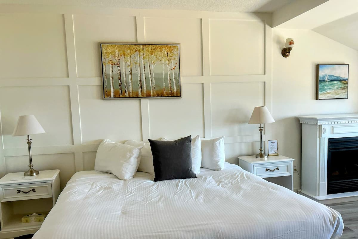 Una camera da letto ben ordinata con un letto grande, due comodini con lampade, un camino e un quadro appeso al muro.