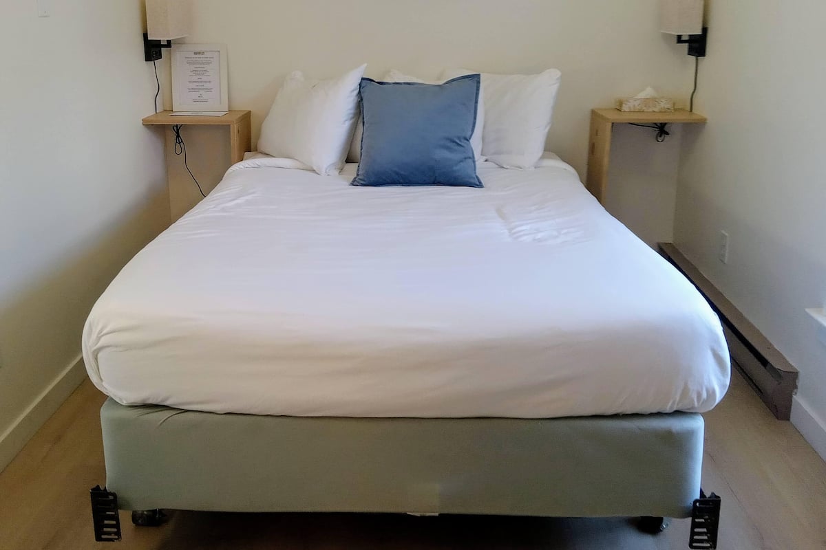 Un letto rifatto con lenzuola bianche e azzurre, due comodini con lampade e un quadro con dei velieri sulla parete.