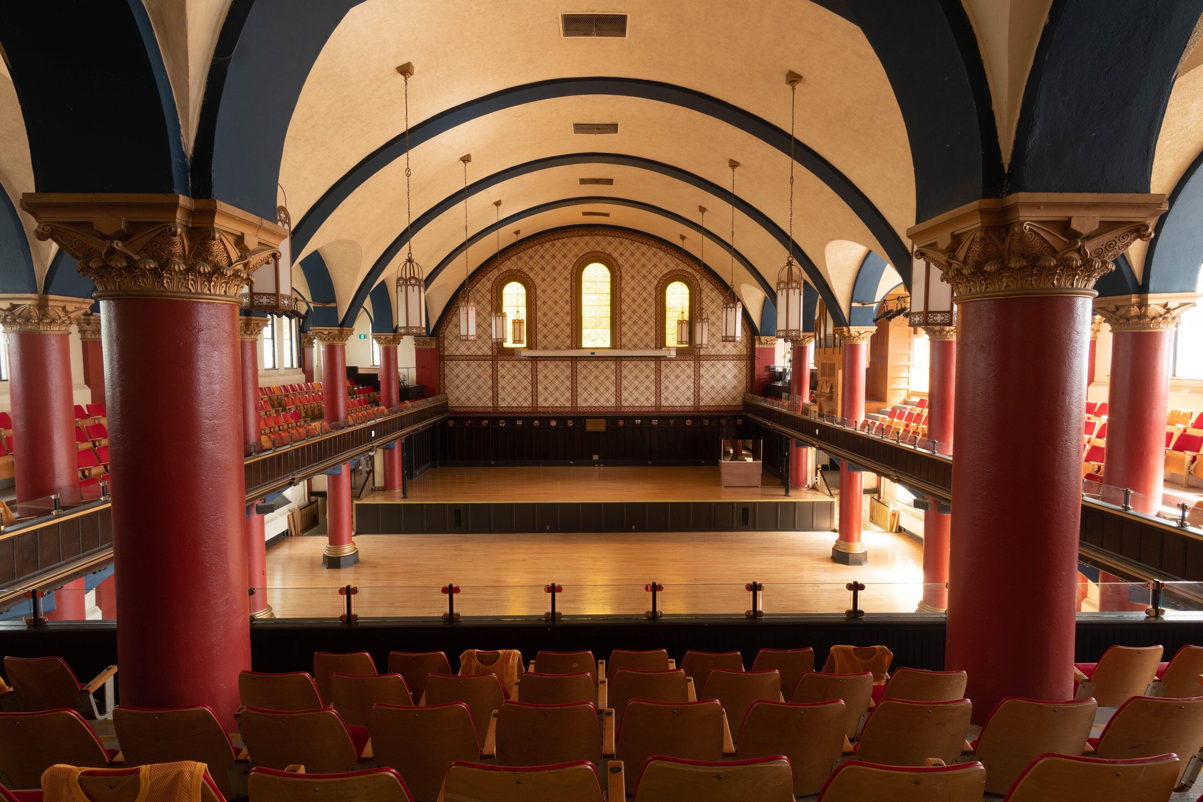 An auditorium with red and gold seating, a balcony, and ornate columns.