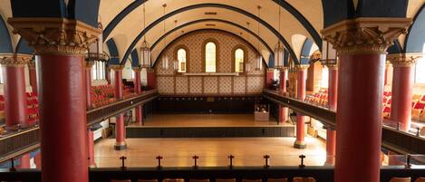 An auditorium with red and gold seating, a balcony, and ornate columns.