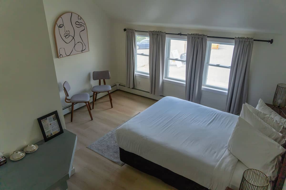Una camera da letto con un letto grande, due poltrone, una finestra con tende e un quadro appeso al muro.