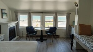 A room with a bed, a table with two chairs, a fireplace, and a view of the sea through large windows. - Hotel Wolfe Island (Wolfe Island)