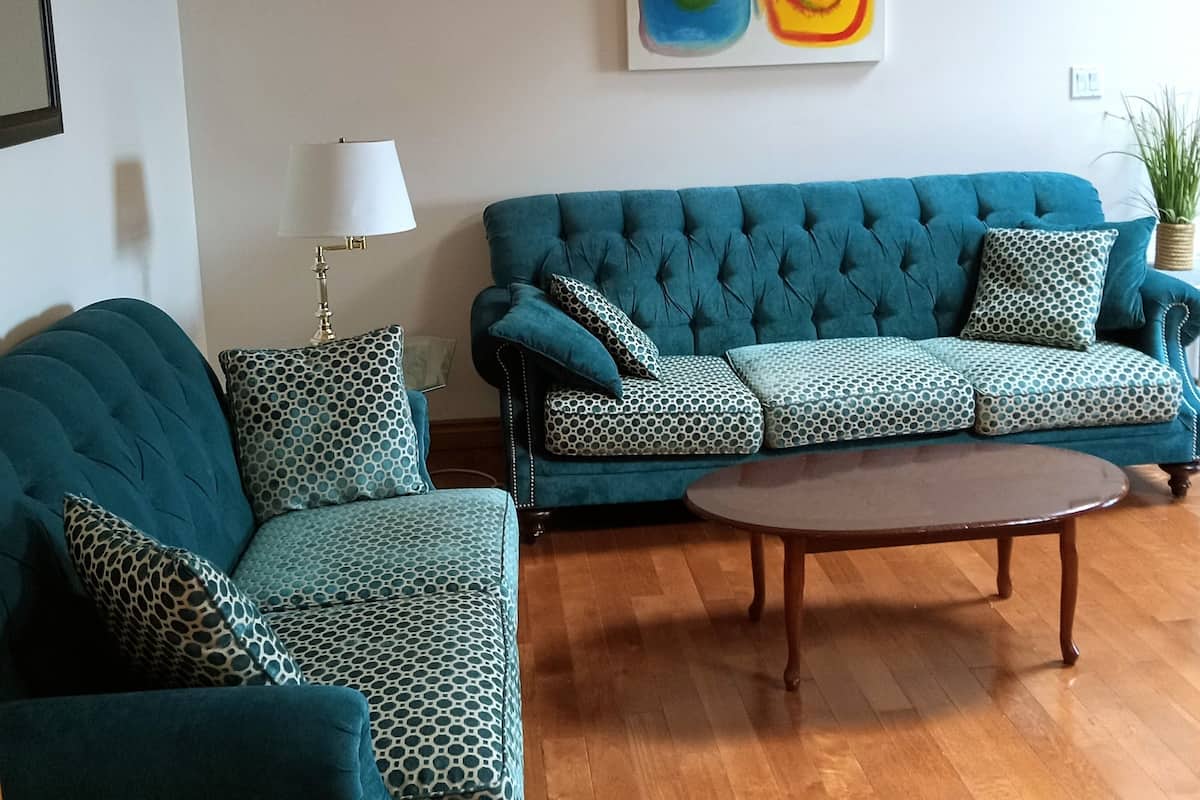 Un soggiorno con un divano color petrolio, cuscini decorati, un tavolino in legno, una lampada da terra e un quadro astratto colorato appeso alla parete.