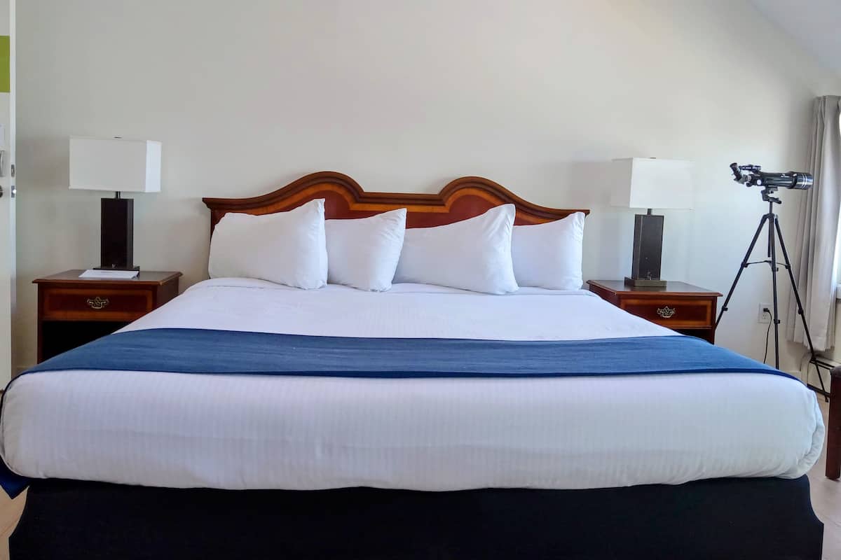 Una camera d'albergo con un letto grande, due comodini con lampade, una fotocamera su un cavalletto e una finestra con tende.