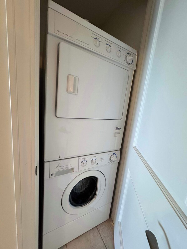 A compact laundry room with a front-loading washing machine and dryer stacked vertically. - Fifth floor suite with views from balcony (Traverse City)