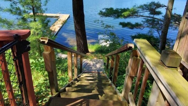 Una escalera de madera que lleva a un muelle sobre un lago rodeado de árboles.