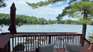 Terraza con sillas de mimbre y una mesa, con vistas a un lago y kayaks.