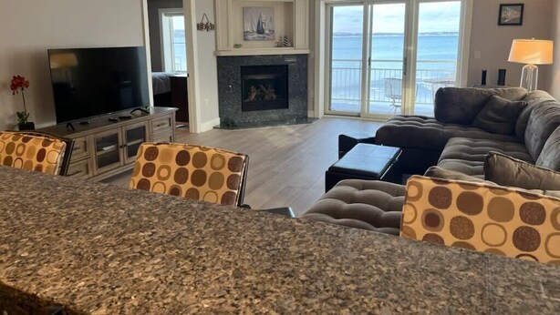 A modern living room with a fireplace, a television, and a large window overlooking the sea.