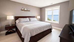 A bedroom with a bed, bedside tables, a TV, a window with a view, and a decorative wall piece.