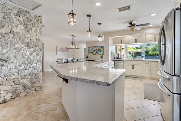 A modern kitchen with a stone accent wall, a large island, stainless steel appliances, and pendant lighting.