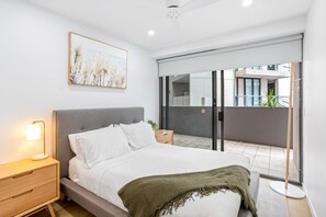 A modern bedroom with a bed, bedside table, and a view of the outside.