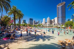 A beach with people, palm trees, and a cityscape with tall buildings in the background.