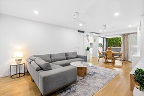 A modern living room with a grey sectional sofa, a round coffee table, and a dining area with a wooden table and chairs.
