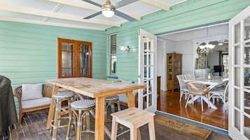 A room with a wooden table and chairs, a ceiling fan, and a view into another room with a dining table and chairs.