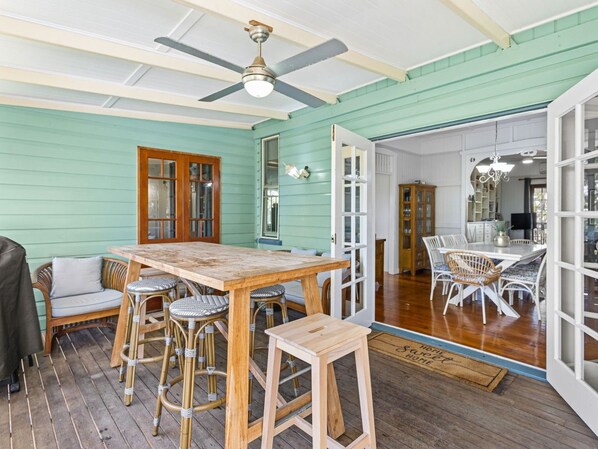 A room with a wooden table and chairs, a ceiling fan, and a view into another room with a dining table and chairs.