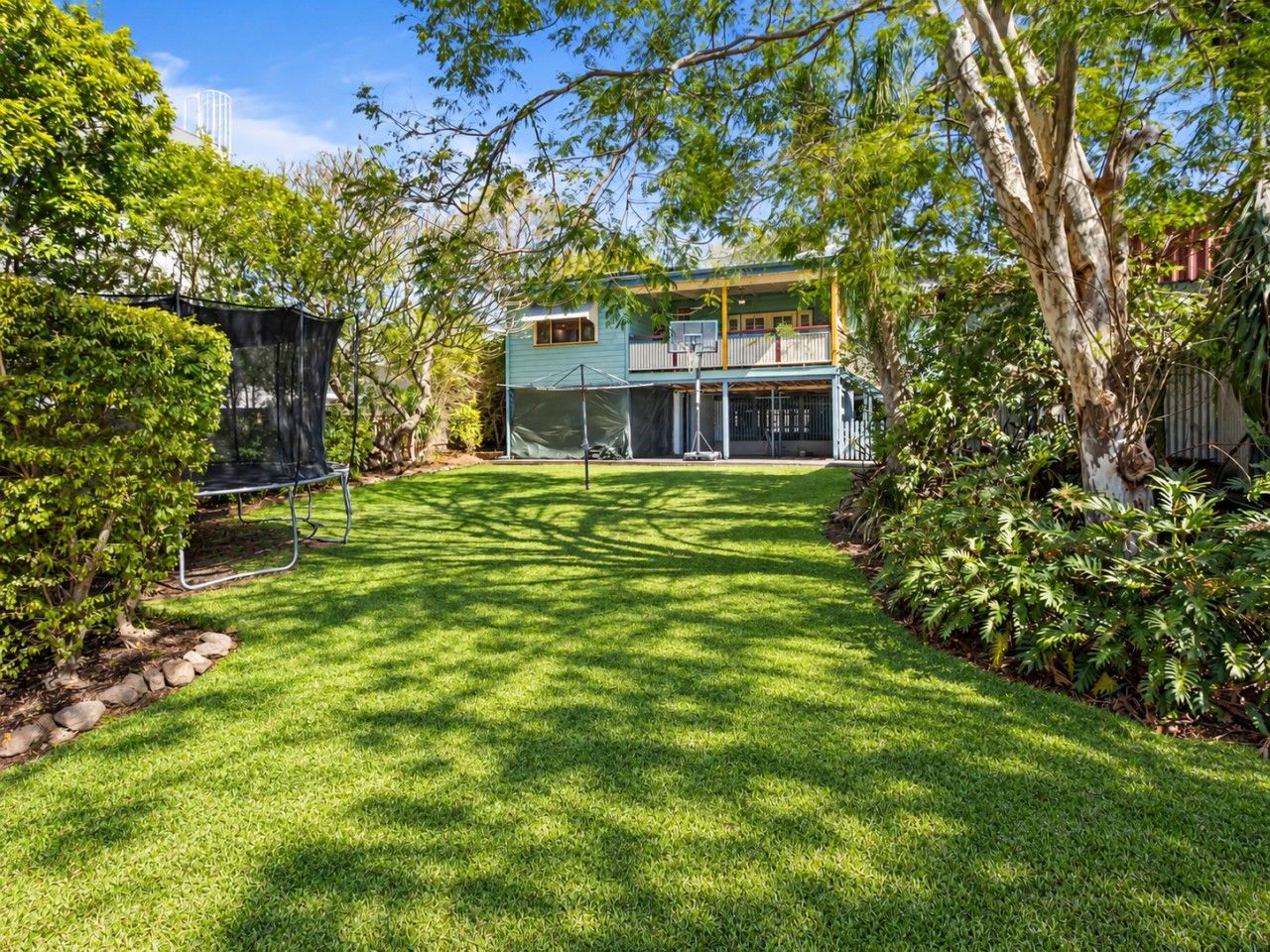 A well-maintained backyard with a lawn, a trampoline, and a two-story house with a balcony.