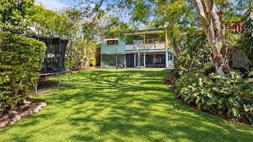 A well-maintained backyard with a lawn, a trampoline, and a two-story house with a balcony.