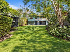 A well-maintained backyard with a lawn, a trampoline, and a two-story house with a balcony.