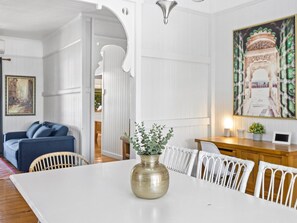 A dining area with a white table, a brass vase with greenery, and a painting of an archway. - Central Location, character home (Grange)