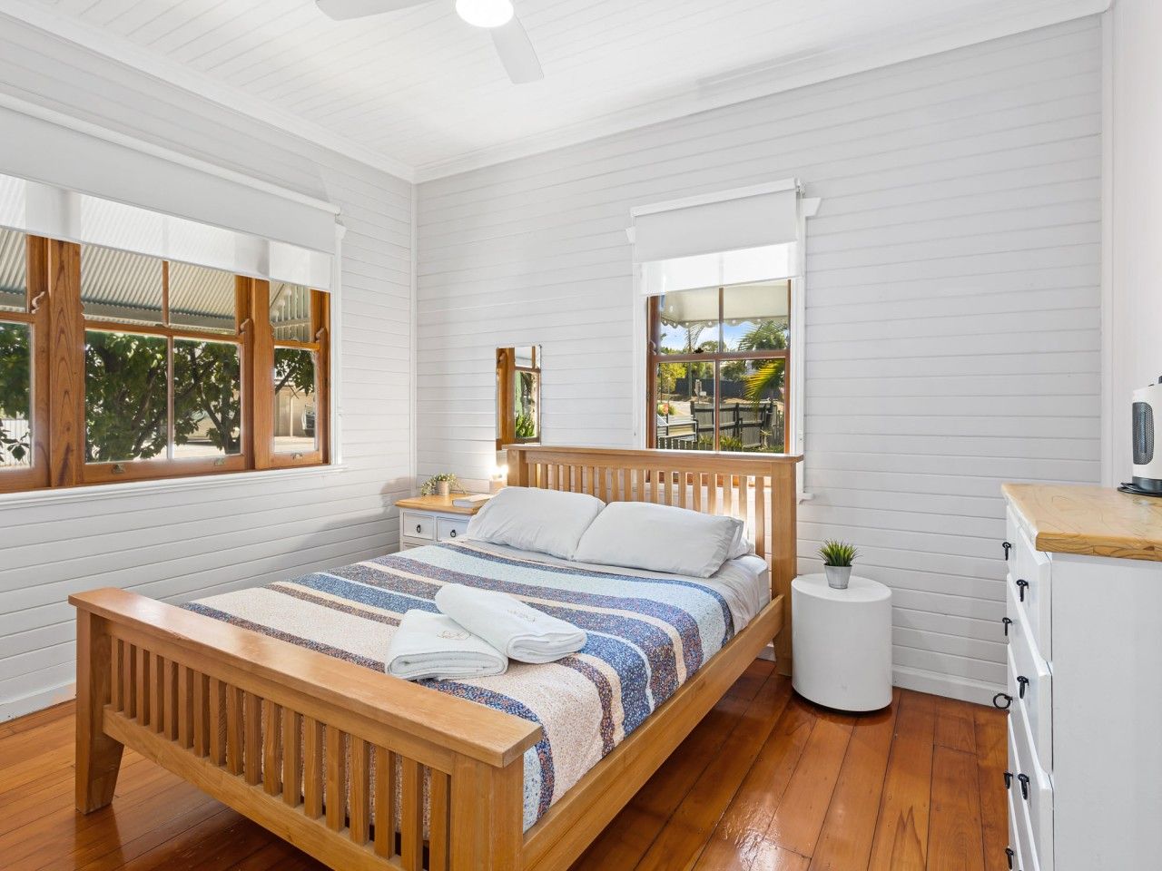 A bedroom with a wooden bed, white walls, and a small round table with a plant.