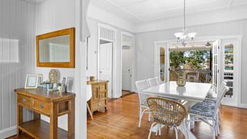 A dining area with a white table and wicker chairs, a wooden sideboard, and a mirror on the wall.